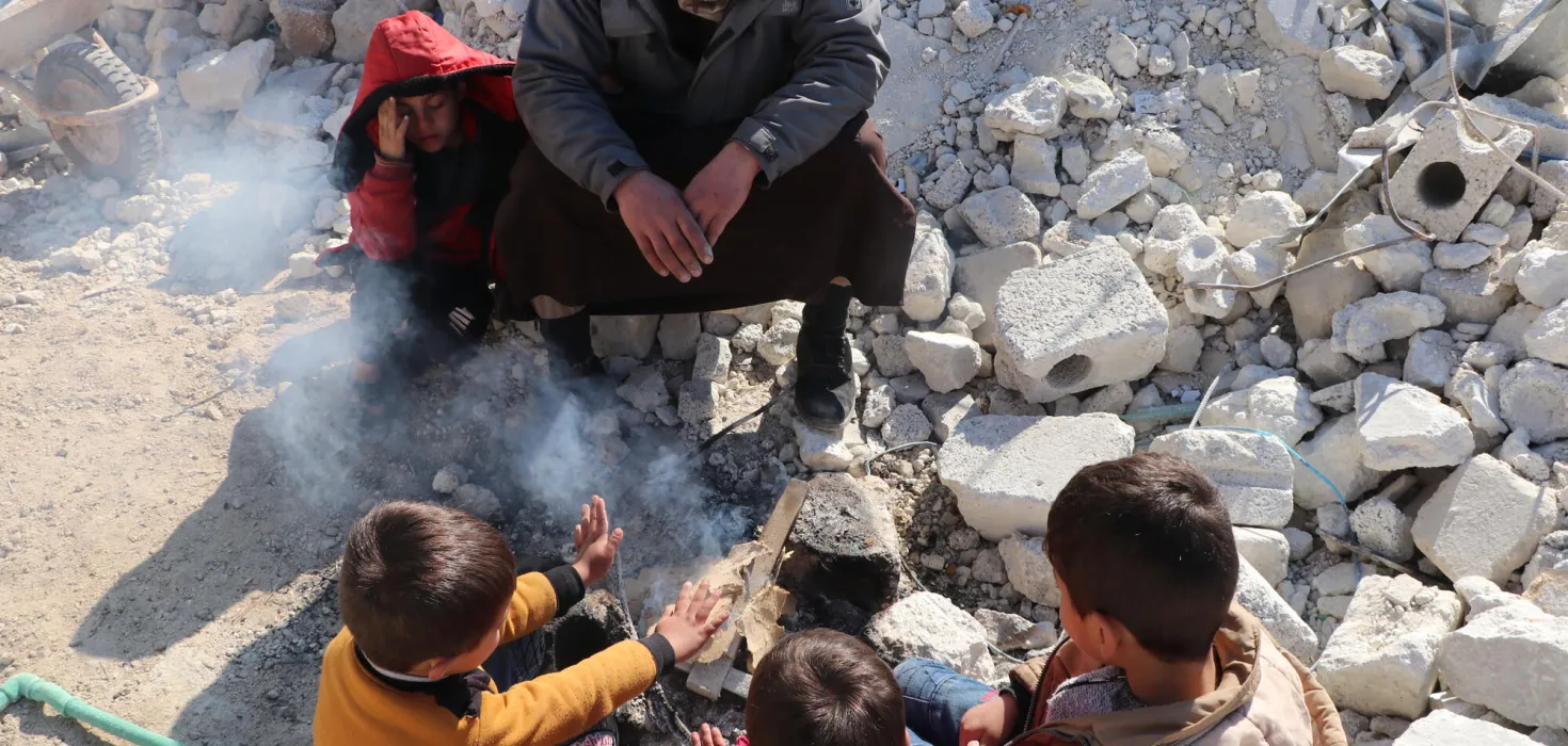Erdbeben in Syrien: Kinder wärmen sich zwischen Trümmern an einem Feuer.
