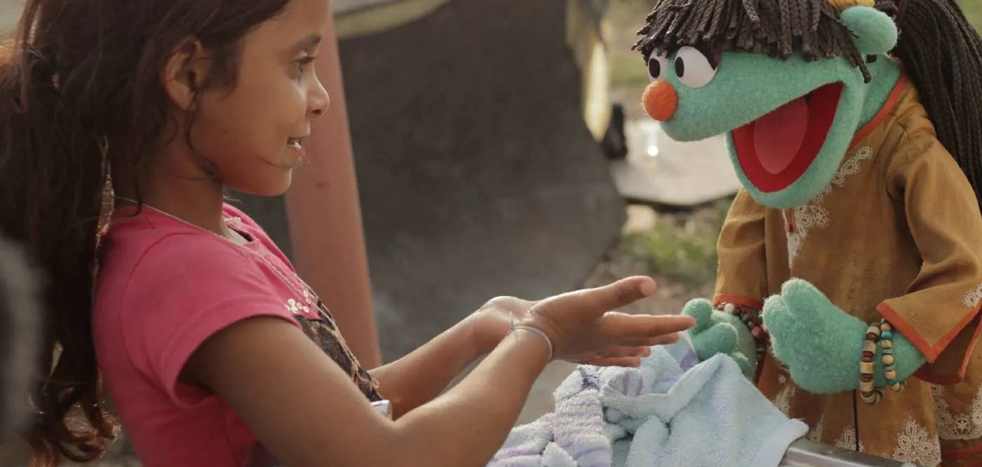 Sesame-Street-Figur Raya übt mit einem syrischen Mädchen das Händewaschen