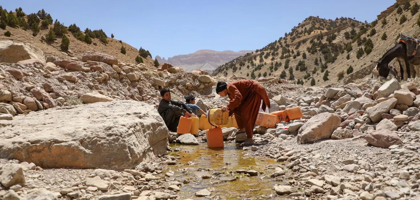 Afghanische Jungen schöpfen Wasser aus einem steinigen Bachbett.