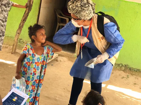 Corona-Gruß und Zuwendung einer World Vision-Mitarbeiterin zu einem Kind in Lateinamerika