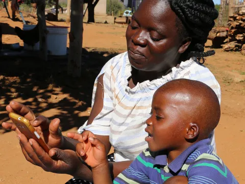 Betty Mhlanga testet mit ihrem Sohn Tamuka in Simbabwe den Audio-Schulunterricht auf dem System VIAMO, unterstützt von World Vision