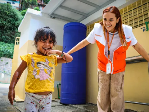 World Vision Mitarbeiterin und ein Mädchen vor einer Handwaschstation in Venezuela