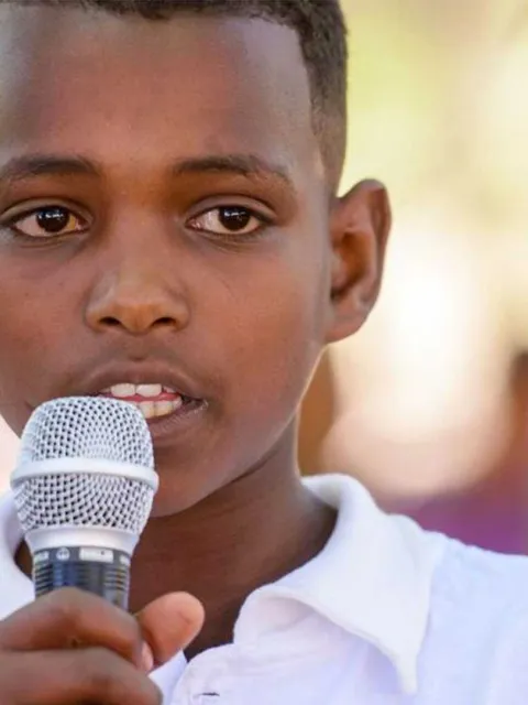 Junge aus Afrika mit Mikrofon in der Hand setzt sich für Kinderrechte ein