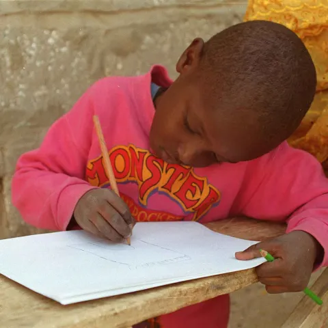 Kleiner Junge der an seinen Hauaufgaben sitzt World Vision