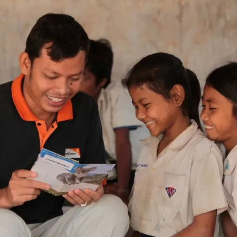 World Vision Mitarbeiter liest zwei Patenkindern in Kambodscha die Post ihrer Paten.