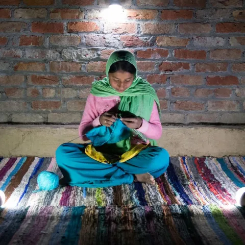 Mädchen in Indien strickt im Schein einer Solarlampe.