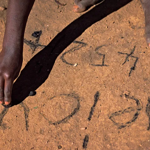 Ein Kind aus Malawi schreibt Vokale und Zahlen in den Sand