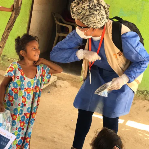 Corona-Gruß und Zuwendung einer World Vision-Mitarbeiterin zu einem Kind in Lateinamerika