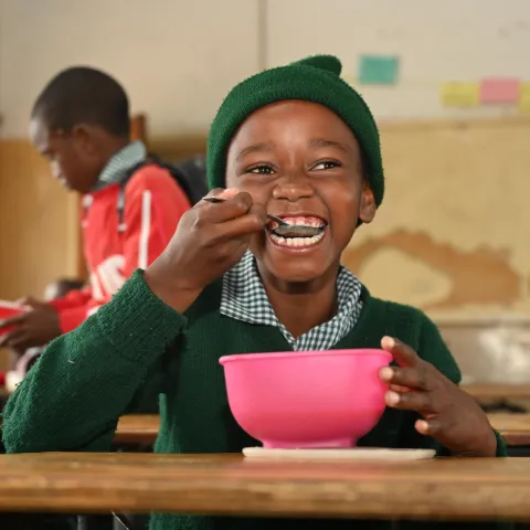 Ein Grundschüler aus dem südlichen Afrika freut sich über seinen Porridge in der Schule.