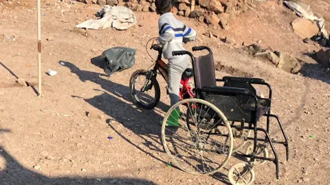 Ein Kind auf dem Fahrrad neben einem Rollstuhl auf Lesbos