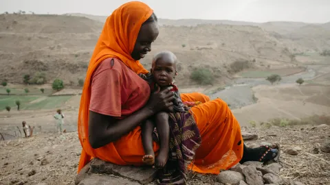 Eine geflüchtete Mutter in Darfur schützt ihr Baby mit einem Schal.