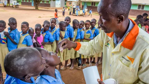 World Vision Mitarbeiter gibt Schulkindern Medizin