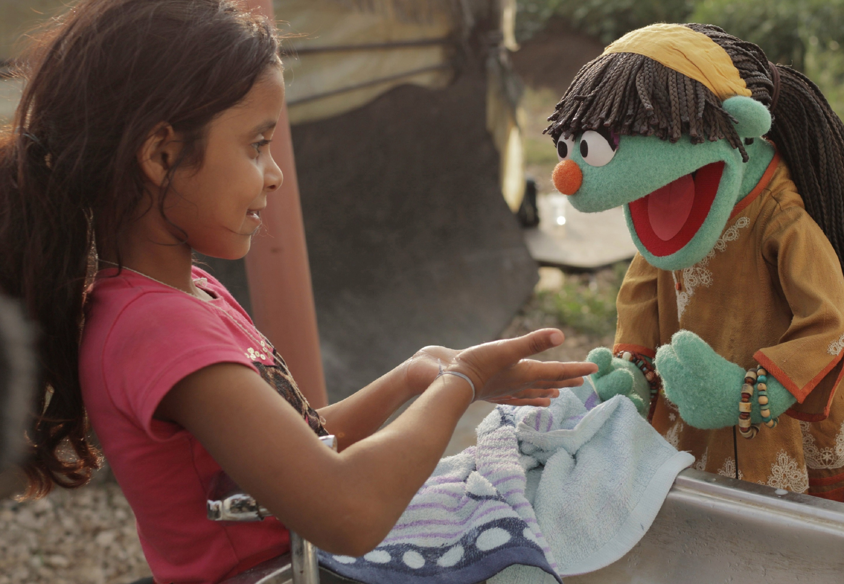 Sesame-Street-Figur Raya übt mit einem syrischen Mädchen das Händewaschen