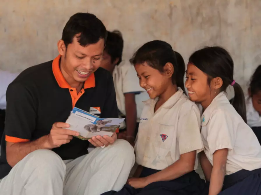 World Vision Mitarbeiter liest zwei Patenkindern in Kambodscha die Post ihrer Paten.