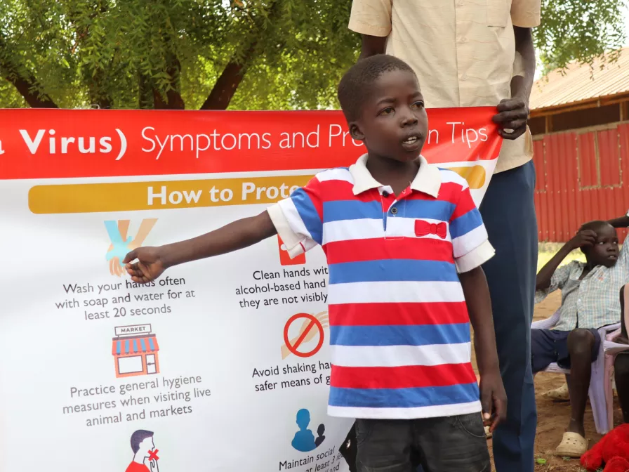 Junge im Südsudan erklärt an einer Tafel Maßnahmen gegen Corona 