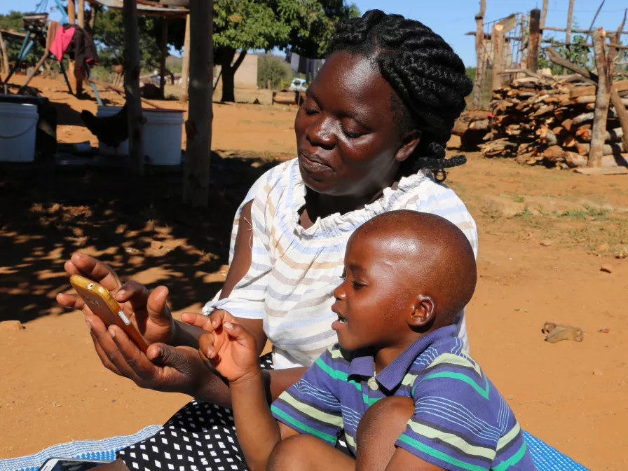 Eine Mutter aus Simbabwe testet mit ihrem Kind die Lektionen für Schulanfänger, die über die Plattform Viamo auf Mobiltelefonen bereit gestellt werden