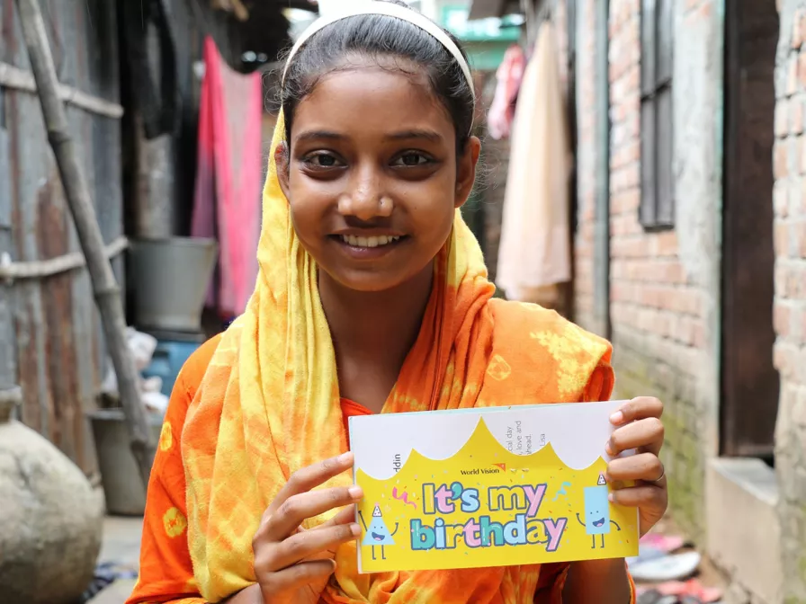 Ein Mädchen aus Indien hält freudig ihre Geburtstagskarte in den Händen