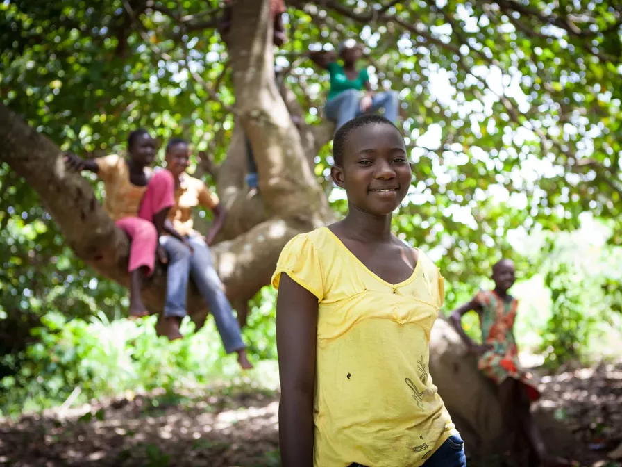 Ein Mädchen steht vor einem Baum in dem Kinder auf Ästen sitzen