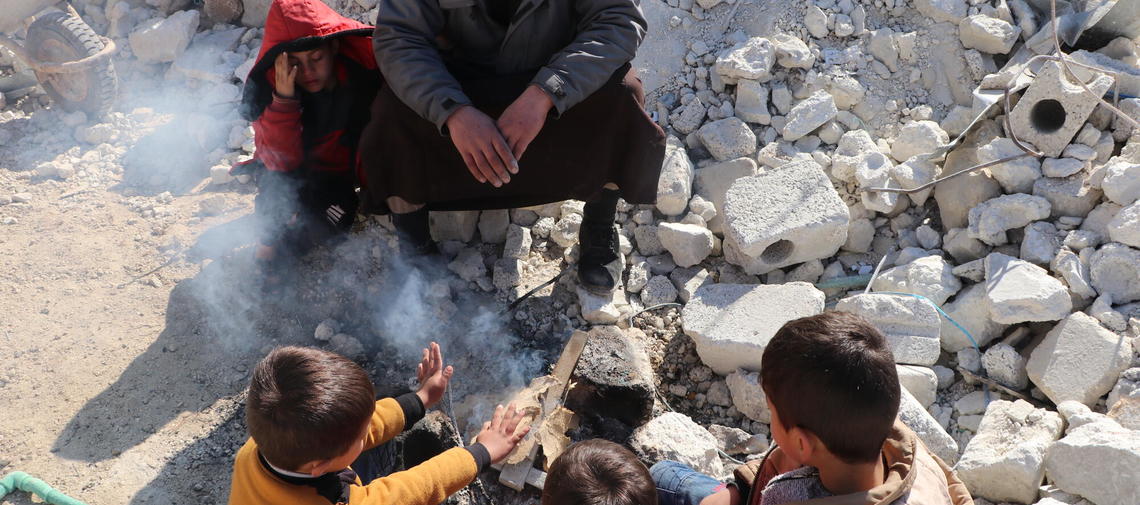 Erdbeben in Syrien: Kinder wärmen sich zwischen Trümmern an einem Feuer.