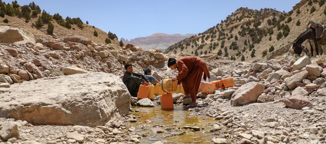 Afghanische Jungen schöpfen Wasser aus einem steinigen Bachbett.