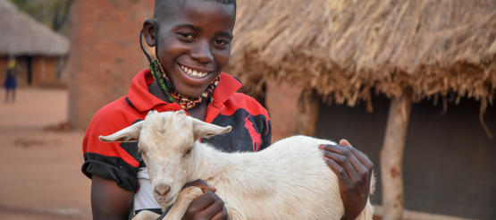 Patenkind Justine aus Sambia hält eine Ziege auf dem Arm.