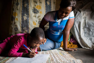 World Vision-Patenkind Praise übt mit Unterstützung ihrer Mutter das Schreiben und Rechnen. 