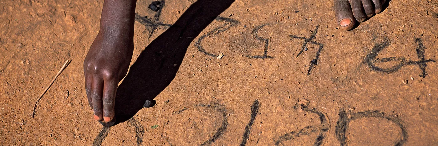 Ein Kind aus Malawi schreibt Vokale und Zahlen in den Sand