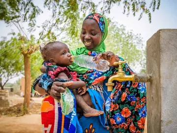 Mutter mit Kleinkind an Trinkstelle