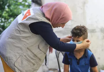 World Vision Mitarbeiterin hilft kleinem Jungen bei dem Anziehen einer Maske