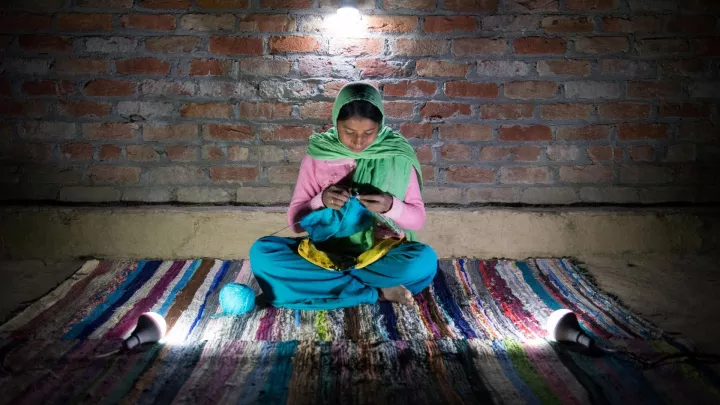 Mädchen in Indien strickt im Schein einer Solarlampe.