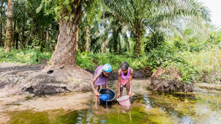 Patenkind Isata schöpft Wasser am Fluss.