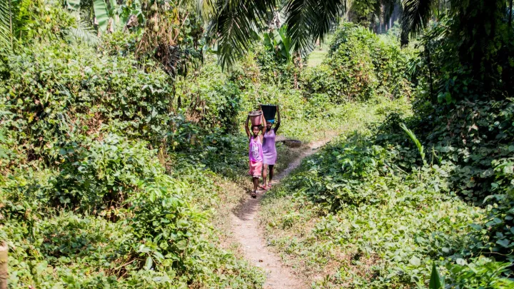 Patenkind Isata trägt den Eimer voller Wasser.
