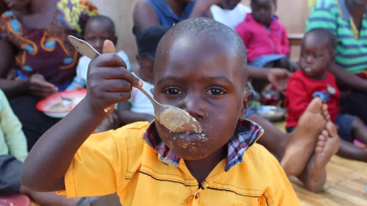 Eine kleiner Junge isst zusammen mit anderem aus dem Dorf.