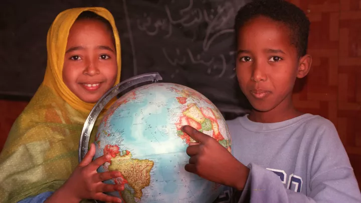 Kinder in Mauretanien zeigen auf einem Globus ihr Heimatland