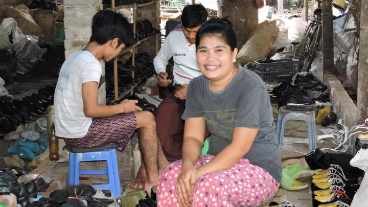 Frau in Myanmar sitzt vor ihrer Schuster-Werkstatt