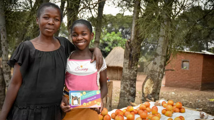 Patenkind Mercy mit ihrer Mutter vor einem Verkaufstisch mit Tomaten