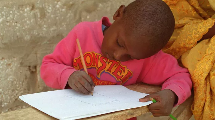 Kleiner Junge der an seinen Hauaufgaben sitzt World Vision