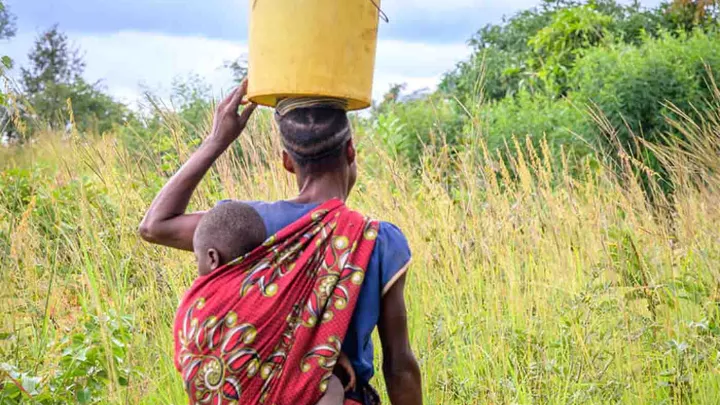 Frau trägt Kind und Wassereimer