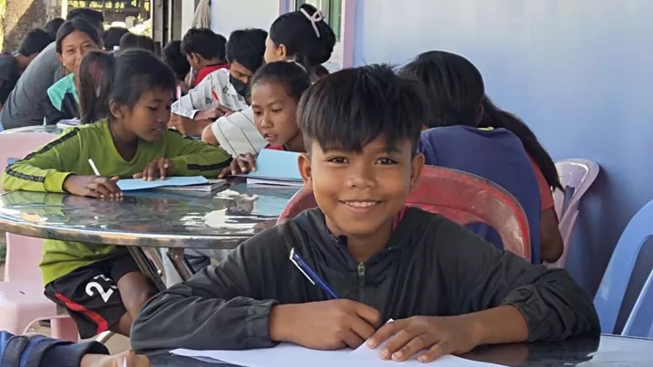 Junge mit anderen Kindern beim Schreiben in Kambodscha