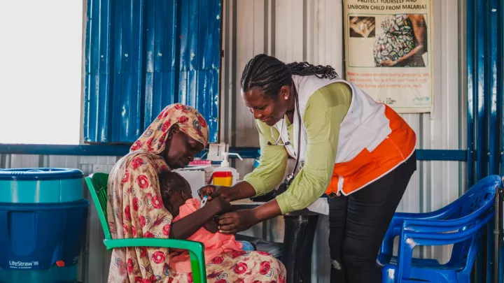 In einer von World Vision betriebenen Nothilfe-Klinik nahe der Grenze zu Sudan misst Hebamme Paula Atimango die Körpertemperatur eines Kleinkindes auf dem Schoß seiner Mutter. Foto: Andre Guardiola / World Vision