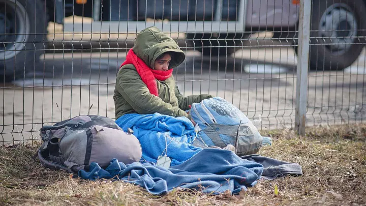 Ukrainisches Flüchtlingskind sitzt in Decke gehüllt an einem Grenzzaun