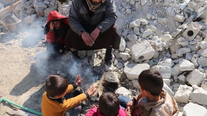 Kinder, die das verheerende Erdbeben im syrisch-türkischen Grenzgebiet überlebt haben, wärmen sich zwischen Trümmern an einem Feuer.