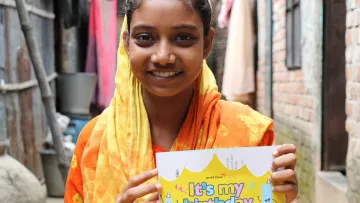 Mädchen aus Indien hält freudig ihre Geburtstagskarte von ihrem Paten in den Händen.