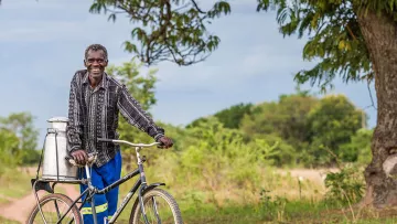 Farmer in Ruanda mit Fahrrad und Milchkanne unterwegs zum Markt