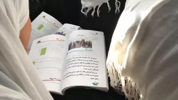 Hilf als Kindheitsretter den Kindern in Afghanistan: Zwei Mädchen lesen in ihren Schulbüchern