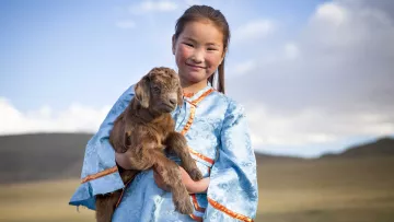 Mädchen in der Mongolei mit Schaf auf dem Arm
