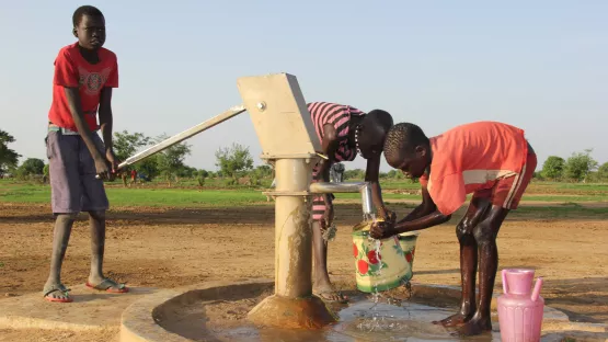 Kinder waschen sich an einem Brunnen.