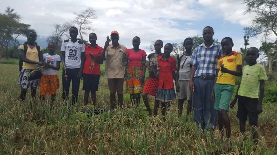 Eine Gruppe an Schülern und ihre Lehrer auf dem Feld, auf dem sie ihr Gemüse für das Schulessen anbauen