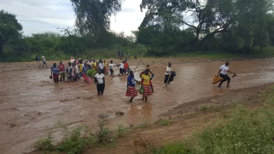 Eine Frauengruppe durchqueren einen Fluss, der vor wenigen Minuten noch ein trockenes Flussbett war.