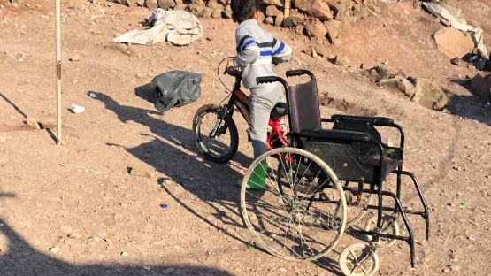 Ein Kind auf dem Fahrrad neben einem Rollstuhl auf Lesbos